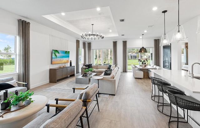 living room featuring a notable chandelier, a tray ceiling, and sink