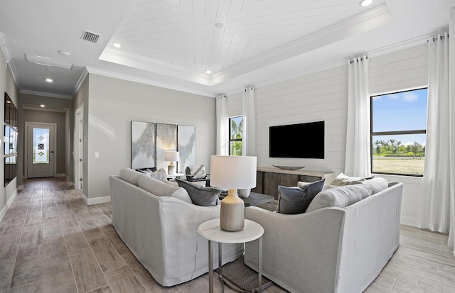 living area featuring light wood finished floors, visible vents, baseboards, ornamental molding, and a tray ceiling