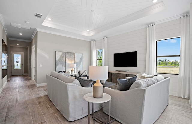 living room featuring a raised ceiling, a healthy amount of sunlight, and crown molding