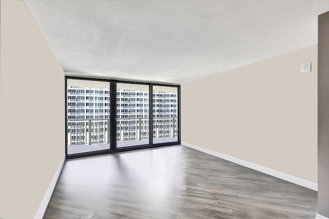 unfurnished room with a textured ceiling, a wall of windows, and dark wood-type flooring