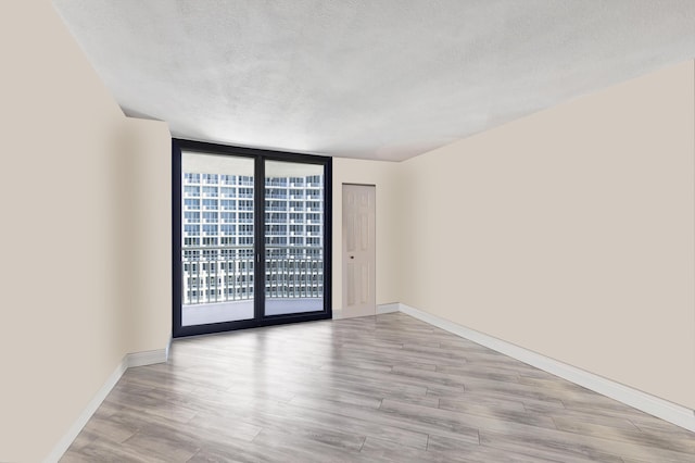 spare room featuring floor to ceiling windows, light hardwood / wood-style flooring, and a textured ceiling