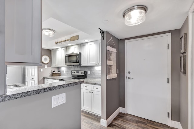 kitchen with light stone countertops, appliances with stainless steel finishes, decorative backsplash, kitchen peninsula, and white cabinetry