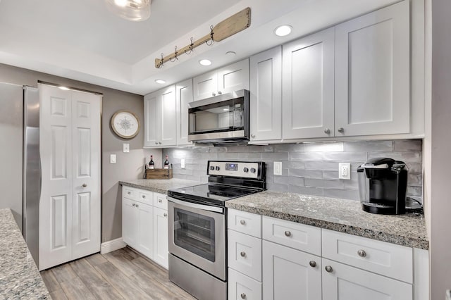 kitchen with backsplash, light stone countertops, light wood-type flooring, white cabinetry, and stainless steel appliances