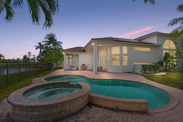 pool at dusk featuring an in ground hot tub and a patio area