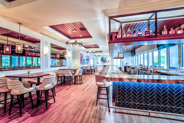 bar featuring ornamental molding, a tray ceiling, hardwood / wood-style flooring, and decorative light fixtures