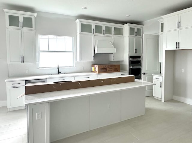 kitchen featuring white cabinetry, a center island, stainless steel double oven, and custom range hood