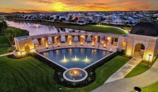 pool at dusk featuring a water view, a yard, and a patio