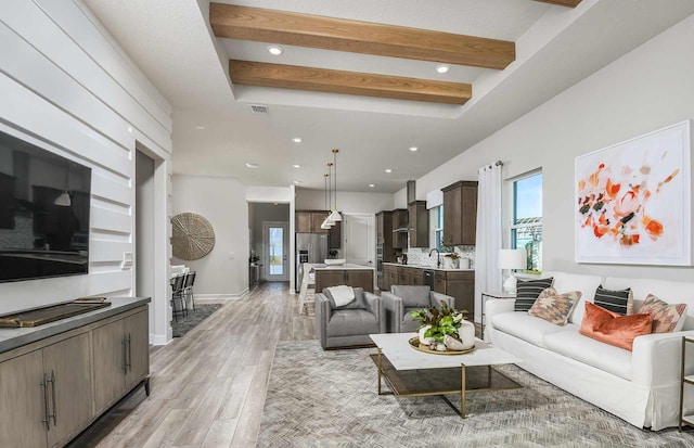 living room featuring beamed ceiling, sink, and light hardwood / wood-style flooring