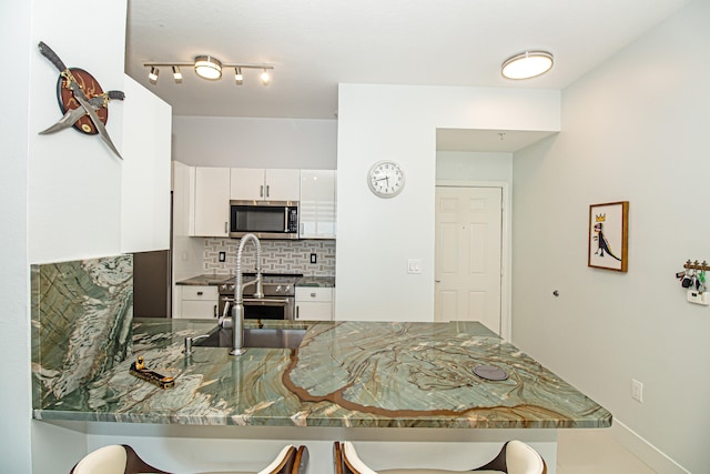 kitchen featuring tasteful backsplash, kitchen peninsula, white cabinets, and stainless steel appliances