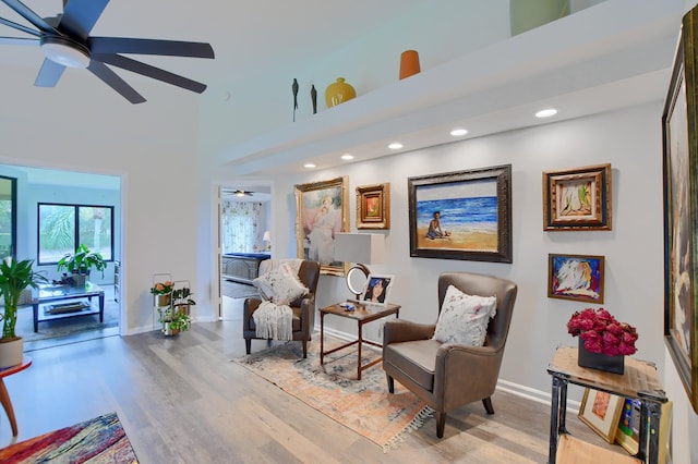 living area featuring a high ceiling, light wood-type flooring, and ceiling fan