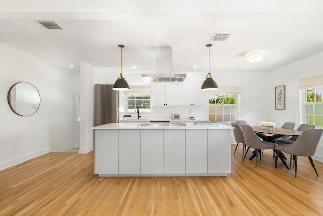 kitchen featuring light wood-type flooring, island range hood, white cabinetry, and hanging light fixtures