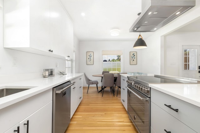 kitchen with wall chimney range hood, appliances with stainless steel finishes, decorative light fixtures, light hardwood / wood-style floors, and white cabinetry