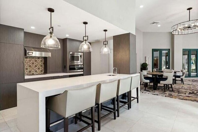 kitchen with appliances with stainless steel finishes, french doors, hanging light fixtures, and a kitchen island with sink