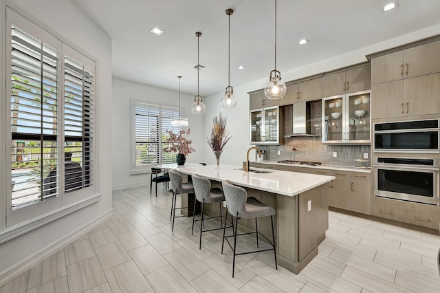 kitchen featuring pendant lighting, a breakfast bar, a kitchen island with sink, sink, and wall chimney exhaust hood