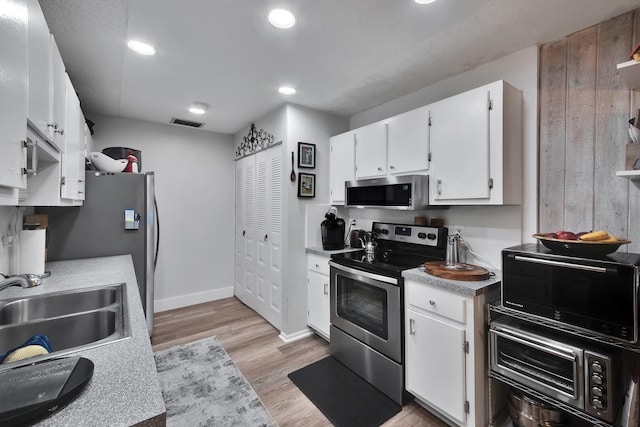 kitchen with white cabinets, appliances with stainless steel finishes, light wood-type flooring, and sink