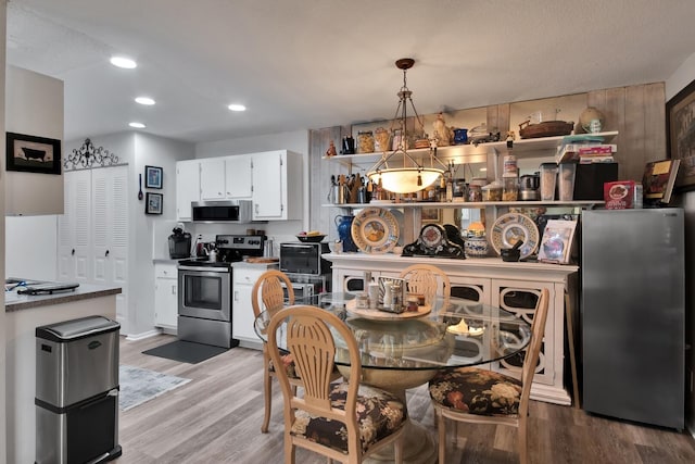 kitchen featuring white cabinets, decorative light fixtures, light hardwood / wood-style floors, and appliances with stainless steel finishes