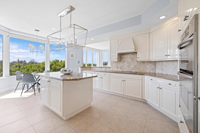 kitchen featuring custom range hood, stone counters, a center island, white cabinetry, and hanging light fixtures