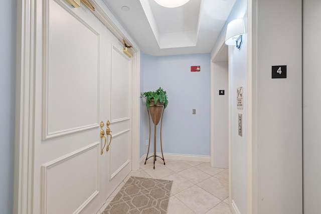 corridor with a tray ceiling and light tile patterned flooring