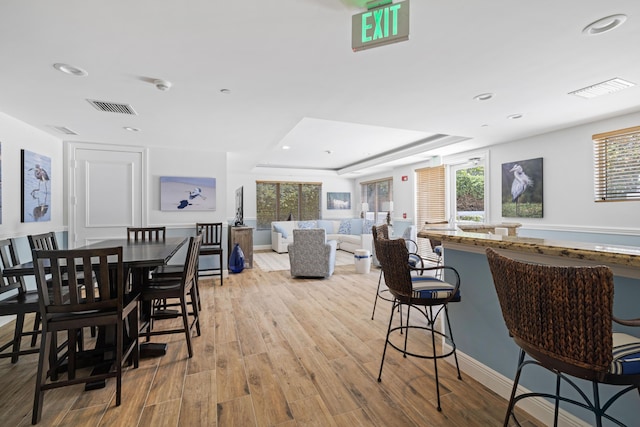 dining area with a raised ceiling, a healthy amount of sunlight, and light wood-type flooring