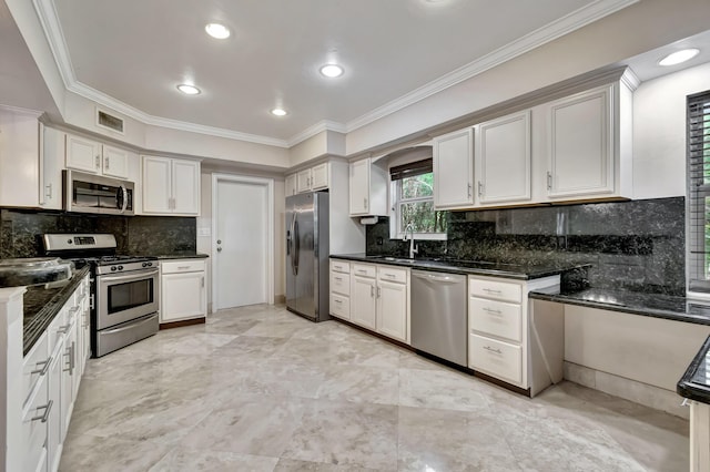 kitchen with stainless steel appliances, white cabinetry, ornamental molding, and dark stone counters