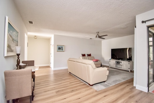 living room featuring ceiling fan, a textured ceiling, and light hardwood / wood-style flooring