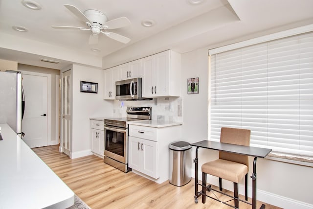 kitchen featuring light hardwood / wood-style flooring, ceiling fan, appliances with stainless steel finishes, white cabinetry, and backsplash