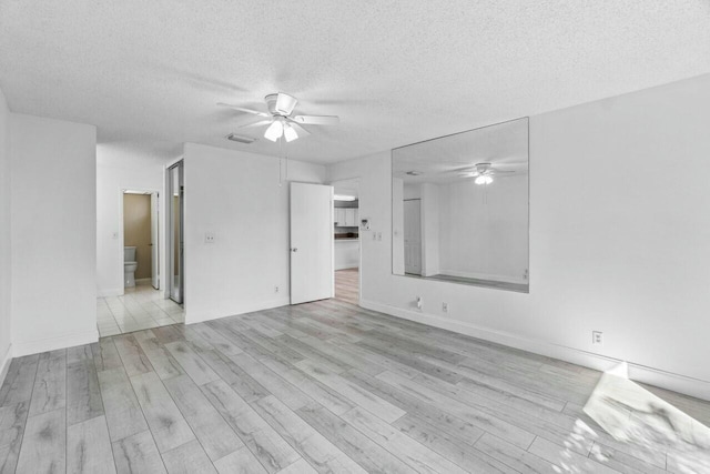 unfurnished room with a textured ceiling, light wood-type flooring, and ceiling fan