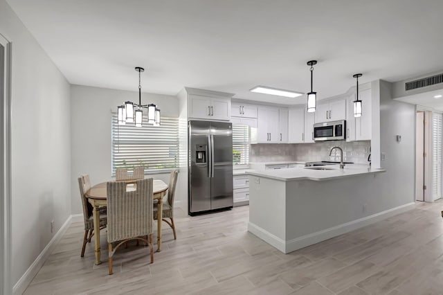 kitchen featuring visible vents, appliances with stainless steel finishes, a peninsula, light countertops, and backsplash