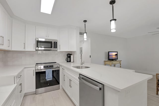 kitchen featuring tasteful backsplash, a peninsula, stainless steel appliances, white cabinetry, and a sink