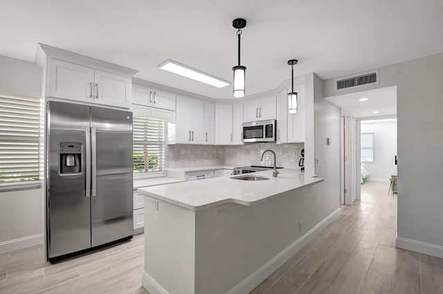 kitchen with visible vents, a peninsula, a sink, stainless steel appliances, and backsplash