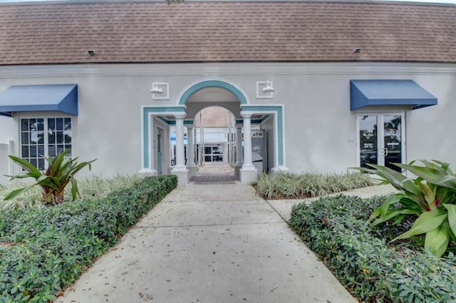 property entrance featuring stucco siding, a shingled roof, and french doors