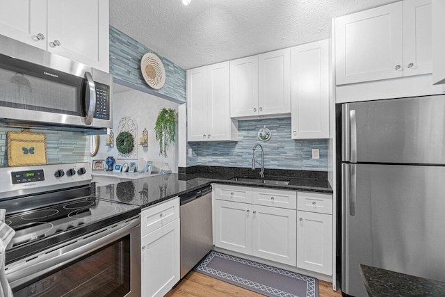 kitchen featuring a textured ceiling, a sink, white cabinetry, appliances with stainless steel finishes, and dark stone countertops