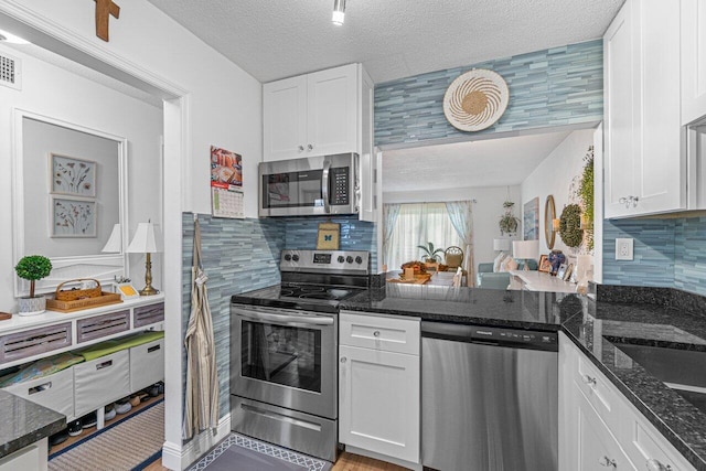 kitchen featuring white cabinets, stainless steel appliances, and dark stone countertops