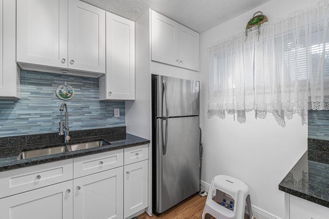 kitchen featuring white cabinets, stainless steel fridge, sink, light hardwood / wood-style flooring, and dark stone countertops