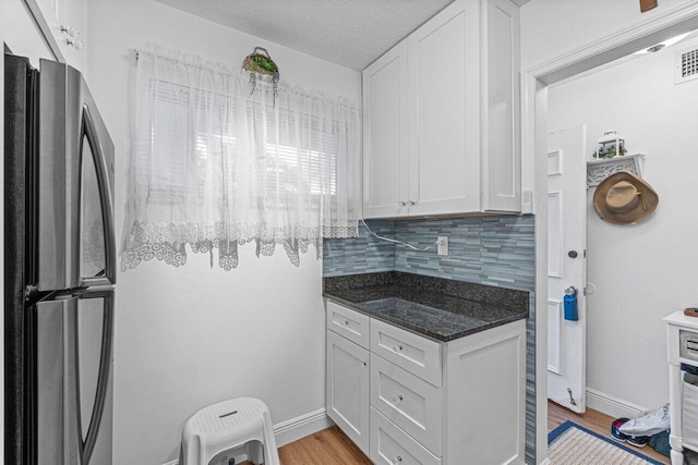 kitchen with white cabinets, backsplash, light hardwood / wood-style flooring, and stainless steel fridge