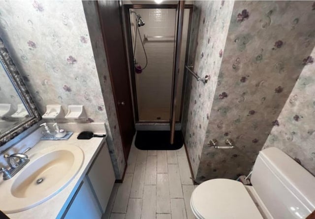 bathroom with wood-type flooring, a shower with shower door, toilet, and vanity