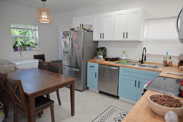 kitchen featuring light tile patterned flooring, backsplash, appliances with stainless steel finishes, blue cabinetry, and decorative light fixtures