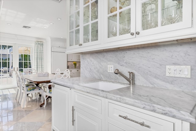 kitchen with light stone counters, white cabinets, glass insert cabinets, and a sink