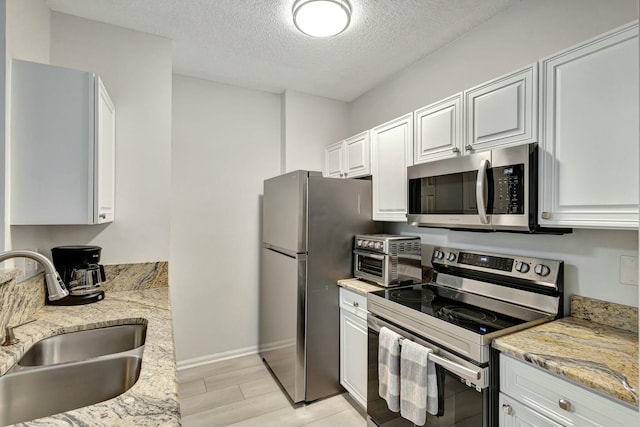 kitchen with sink, a textured ceiling, appliances with stainless steel finishes, light stone counters, and white cabinetry