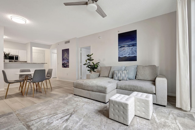 living room featuring ceiling fan, light hardwood / wood-style flooring, and a textured ceiling