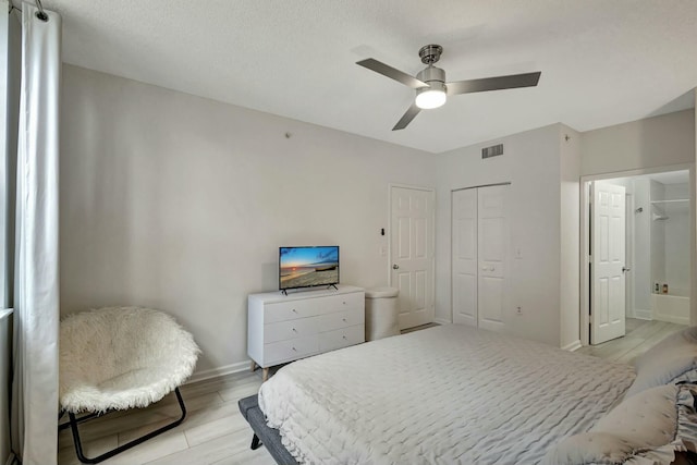 bedroom with light wood-type flooring, ensuite bathroom, a textured ceiling, ceiling fan, and a closet