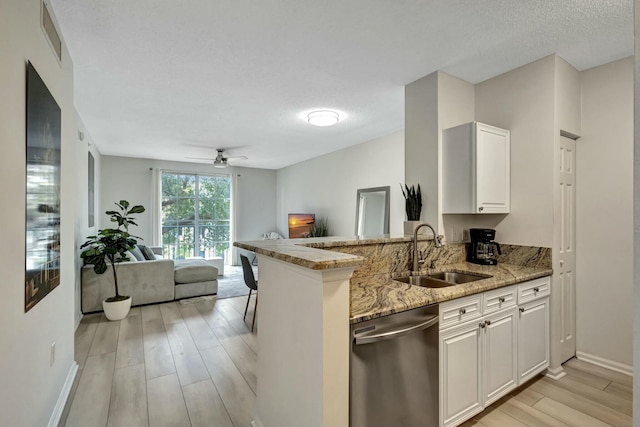 kitchen featuring dishwasher, kitchen peninsula, sink, light stone counters, and white cabinetry