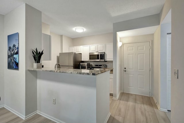 kitchen with white cabinetry, light stone countertops, kitchen peninsula, appliances with stainless steel finishes, and light wood-type flooring