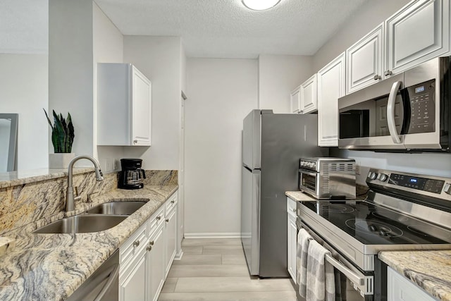 kitchen featuring light stone countertops, sink, a textured ceiling, white cabinets, and appliances with stainless steel finishes