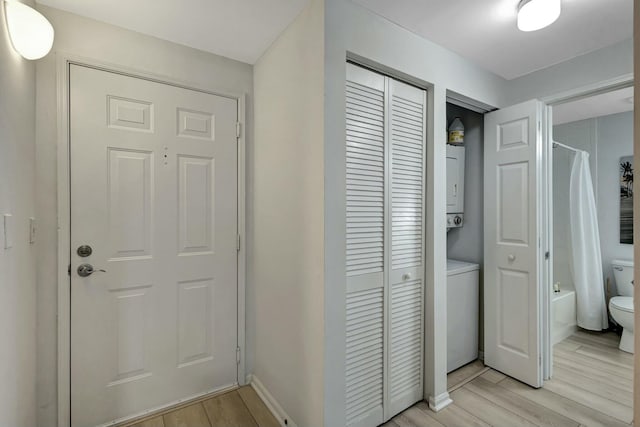 hallway with stacked washer and clothes dryer and light wood-type flooring