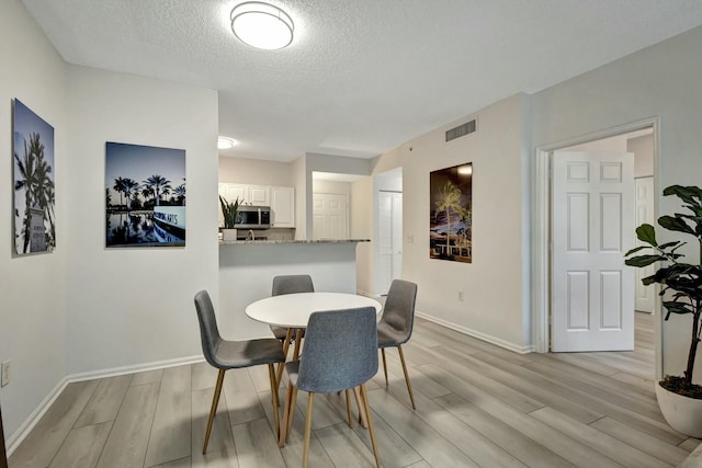 dining area with a textured ceiling and light hardwood / wood-style floors