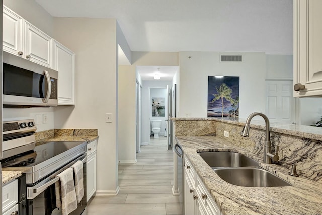 kitchen with light stone countertops, appliances with stainless steel finishes, sink, light hardwood / wood-style flooring, and white cabinetry