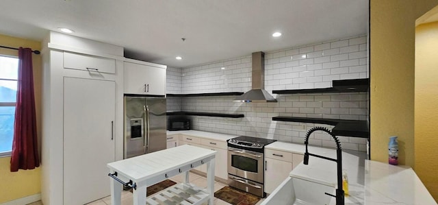 kitchen with decorative backsplash, white cabinets, appliances with stainless steel finishes, and wall chimney exhaust hood