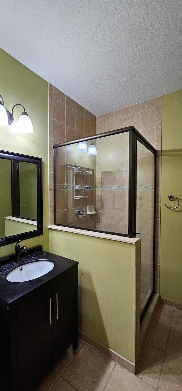 bathroom with a textured ceiling, tiled shower, vanity, and tile patterned flooring