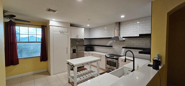 kitchen featuring appliances with stainless steel finishes, white cabinetry, wall chimney range hood, decorative backsplash, and ceiling fan